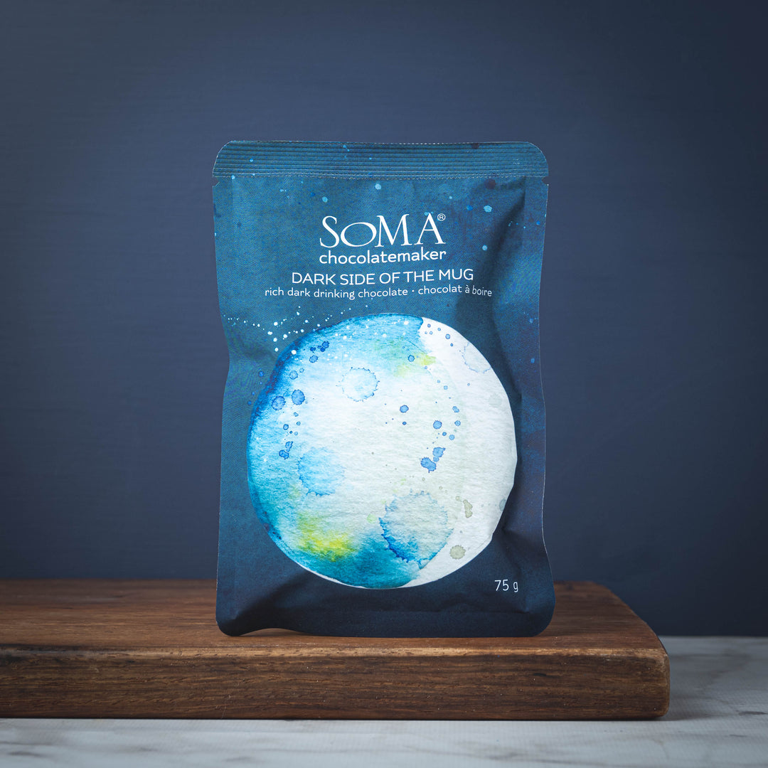 SOMA drinking chocolate packaging on a wooden surface with a dark blue background