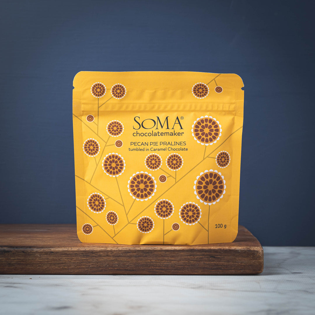 Yellow package of SOMA Pecan Pie Pralines on a wooden boardwith a blue background