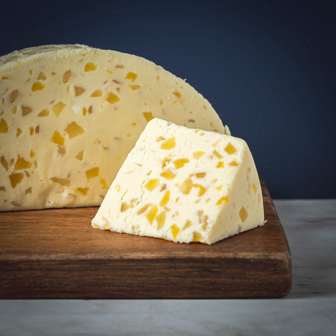 A wedge of White Stilton with Mango and Ginger cheese on a wooden board with a blue background