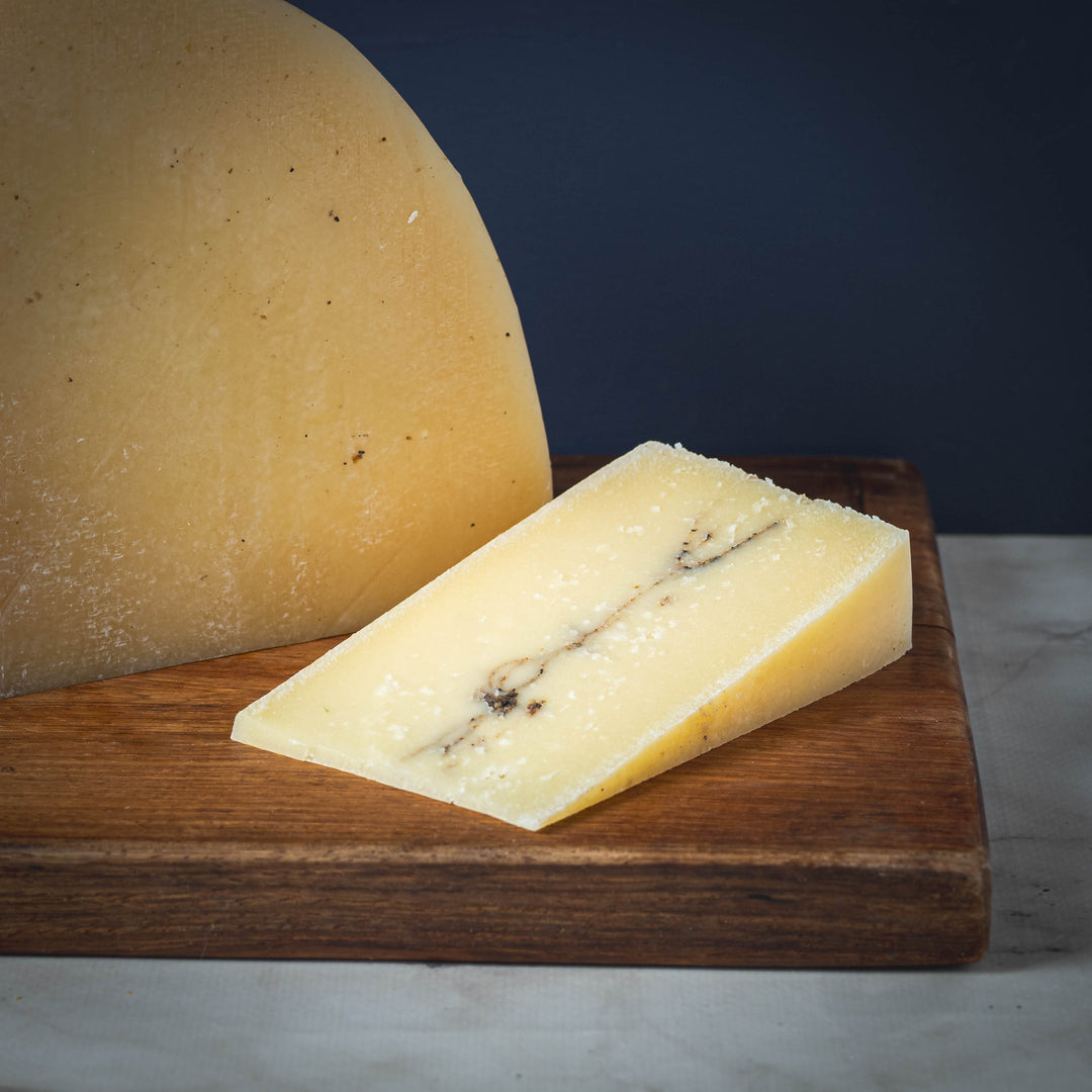 Wheel of Millefoglie al Tartufo cheese with a wedge cut on a wooden board against a dark background