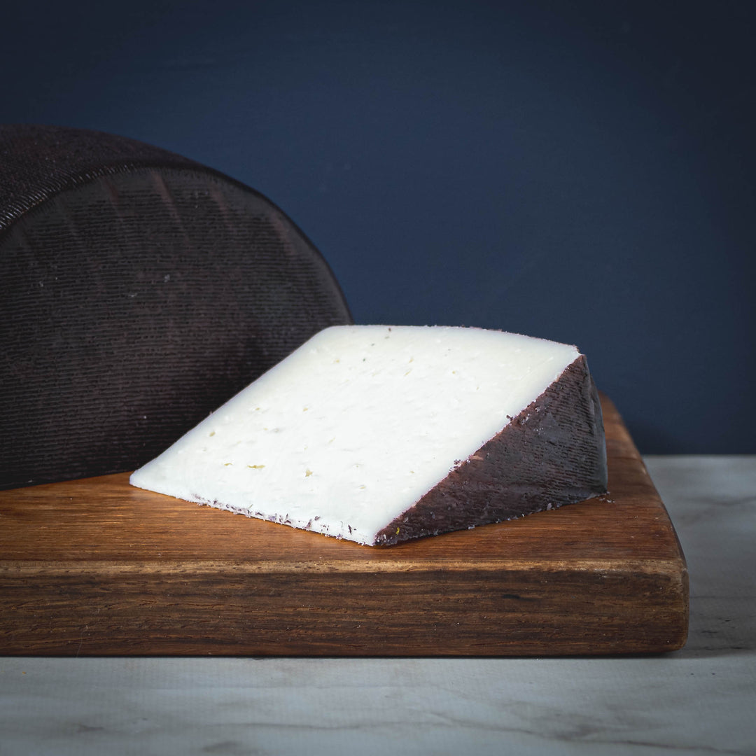 A wedge of Murcia al Vino (aka drunken goat) cheese on a wooden board with a dark background