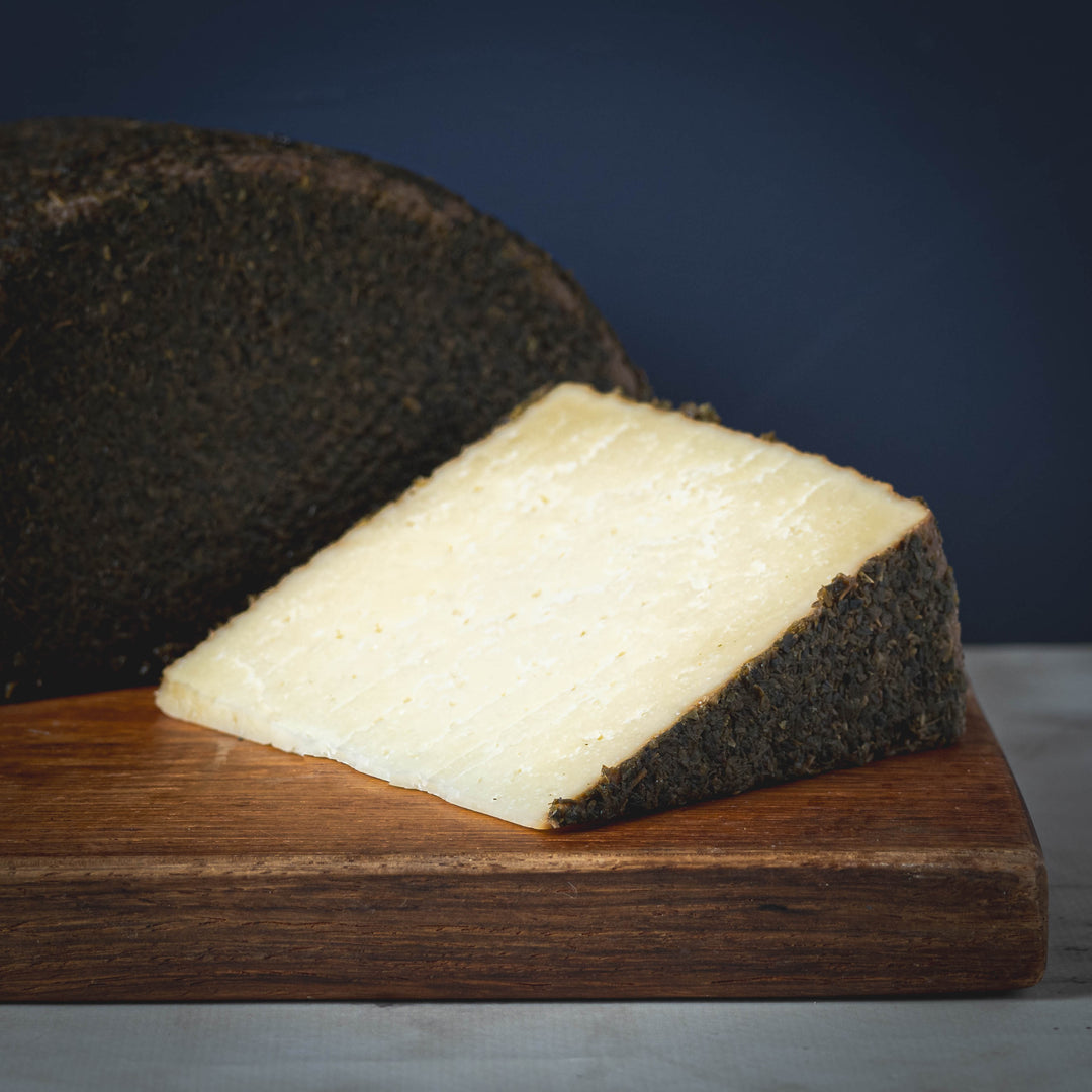 A wedge of Oveja con Oregano y Miel cheese from Spain on a wooden board with a blue background