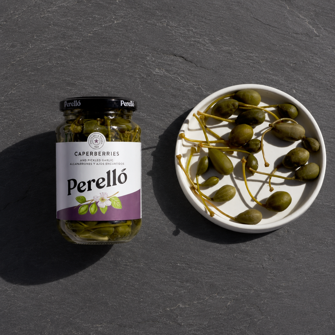 Jar of Perello caperberries and a bowl of caperberries on a dark surface